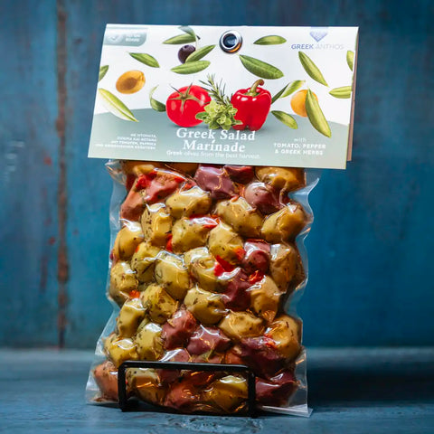 Gemischte Oliven in Greek Salad Marinade im blauen Ambiente – vielfältige mediterrane Oliven in würziger Marinade, perfekt für griechische Salate und Feinschmecker.